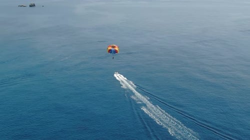 Aerial top view of speed boat towing colorful parachute with person parasailing over deep ocean