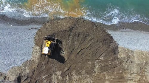 Drone view of dump truck and bulldozer falling asleep on embankment by sea.