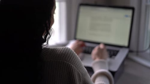 Young woman typing quickly on a laptop computer or tablet with a keyboard - view from behind
