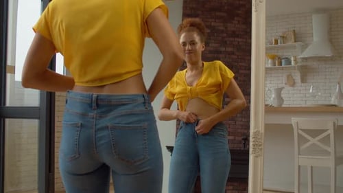 Overweight Black Woman Trying to Button Up Tight Pants in Front of Mirror