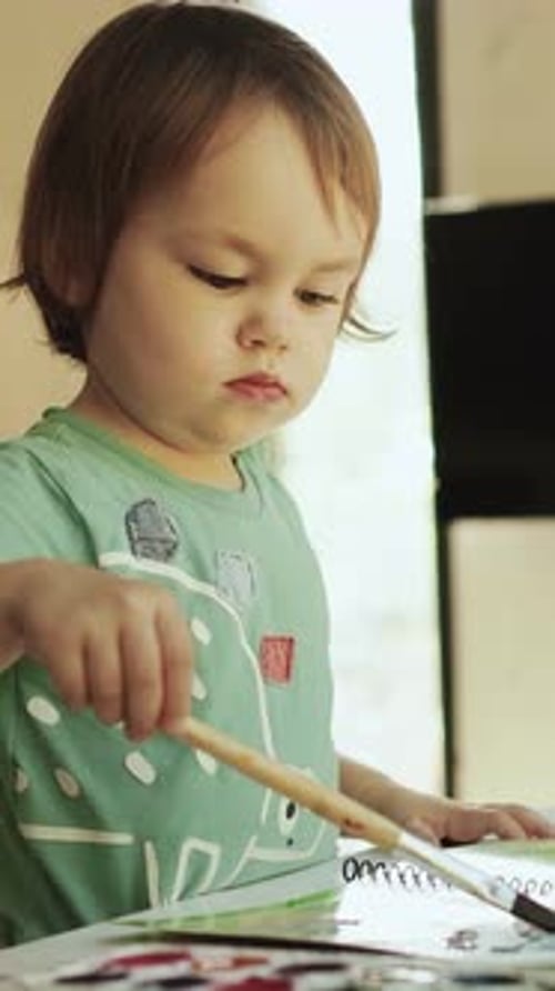 Écran vertical qu'une fille peint à la maison avec un pinceau sur une table dans une pièce lumineuse en l'explorant joyeusement