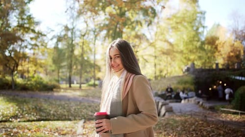 Side View Portrait of Caucasian Beautiful Young Woman Going Forward in Park with Glass of Coffee and