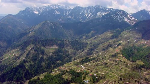 Aerial view over the mountain forest and valley to the icy mountains, Clouds are touching to the top