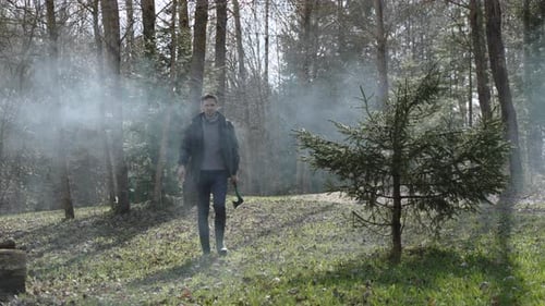 Brutal Caucasian Man with Ax in Hand Walks Through Smoke in Forest