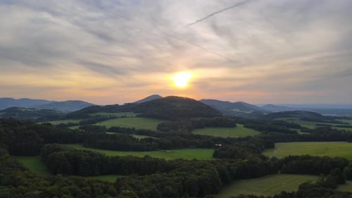 Aerial view of hilly landscape of meadows woods field during sunset on golden sunset background.