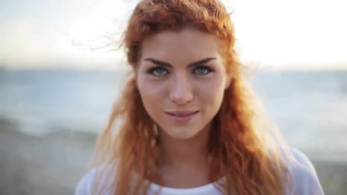 Happy young redhead woman smiles on a sunny beach with slow motion