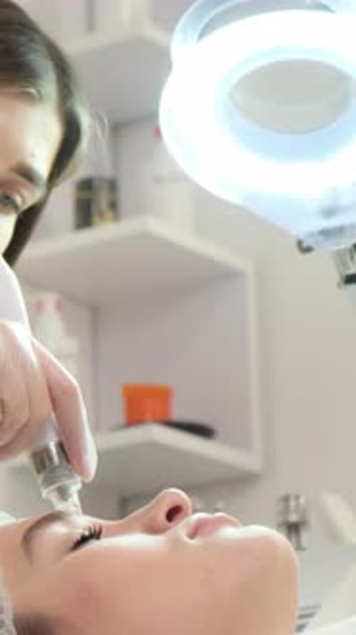 Die Kosmetikerin führt eine Nadelmesotherapie im Gesicht einer Frau durch - Verjüngungsverfahren | Vertikales Video