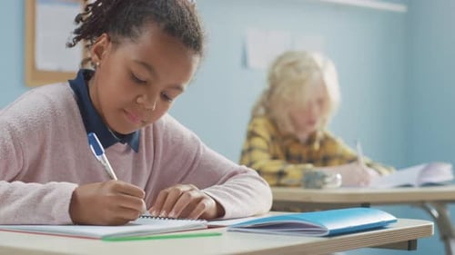 In Elementary School Classroom Brilliant Black Girl Writes in Exercise Notebook, Taking Test and Wr