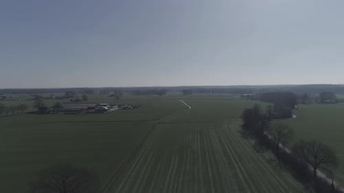 Drohnenaufnahme von Ackerland mit Stadt und Bäumen auf sich und ab.