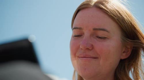 Close Up Of Digital Creator Smiling While Using Phone Under Clear Sky