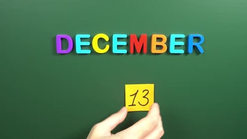 Hand sticking a sticker 13 December calendar day on school board. 13 date of December. Thirteenth