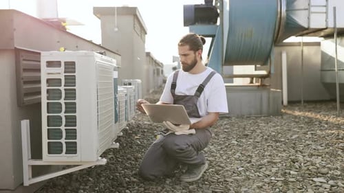 Man Inspecting Air Conditioning Unit With Laptop