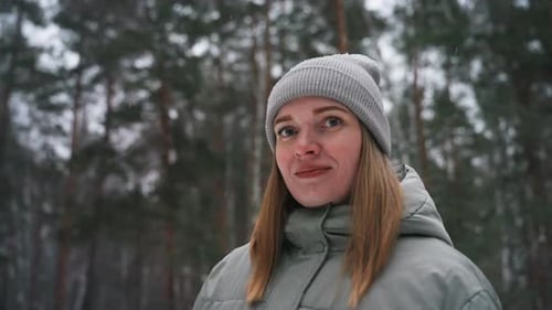 Portrait of Woman in Gray Winter Coat and Knitted Beanie Standing in Snowy Forest