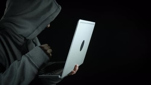 Hooded Person Typing on a Laptop in Dark