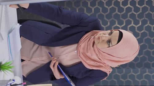 Vertical Video of Muslim business woman in hijab takes and analyzes notes in office.