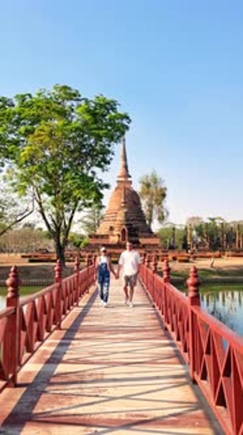 Deux voyageurs se promenant sur un pont en bois menant au temple en admirant le ciel et les arbres aquatiques Sukhothaï, Thaïlande