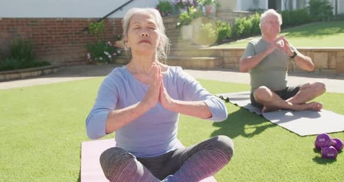 Happy diverse senior couple practicing yoga and meditating on mats in garden