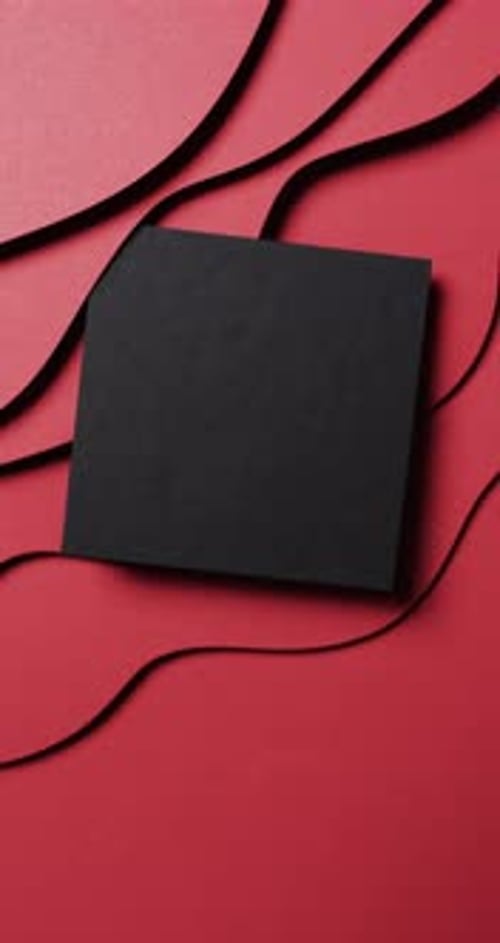 Vertical video of square of black paper on waves cut out and copy space on red background