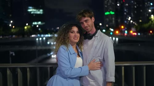 Romantic Young Couple Posing and Hugging on a City Bridge at Night