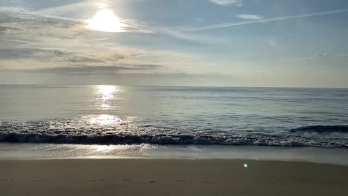 Strandszene in Zeitlupe mit Wellen, die bei Sonnenaufgang am Sommermorgen gegen die Küste rollen