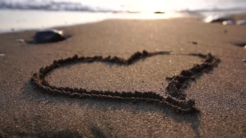 Herzsymbol, gezeichnet auf Strandsand bei schönem Sonnenuntergang, von Meereswellen weggespült, handgezeichnetes Herz auf