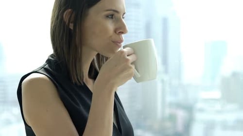 Businesswoman Drinking Coffee And Admire View From Window In Office