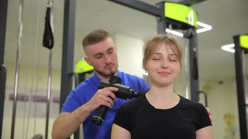 Terapeuta masculino masajeando el cuello de una mujer con una pistola de percusión