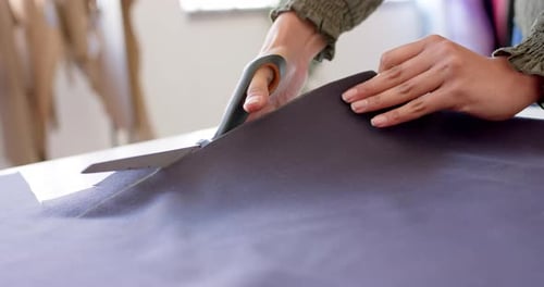 Hände einer birassischen Modedesignerin, die Stoff mit einer Stoffschere auf dem Tisch schneidet, Zeitlupe