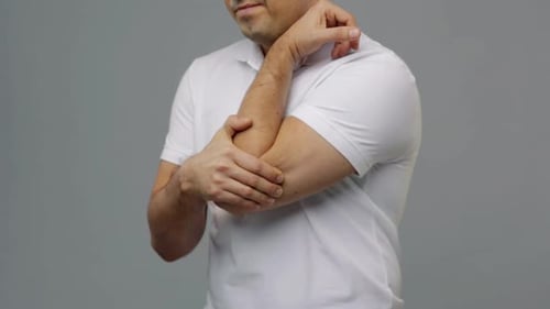 Man rubs his sore elbow in studio setting