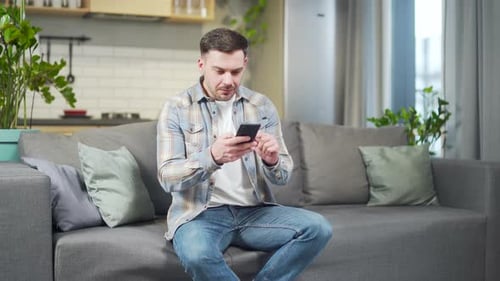 Excited Man Celebrates Phone Success on Living Room Couch