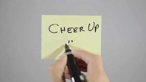 Hand Writes Cheer Up Message on Yellow Notepad
