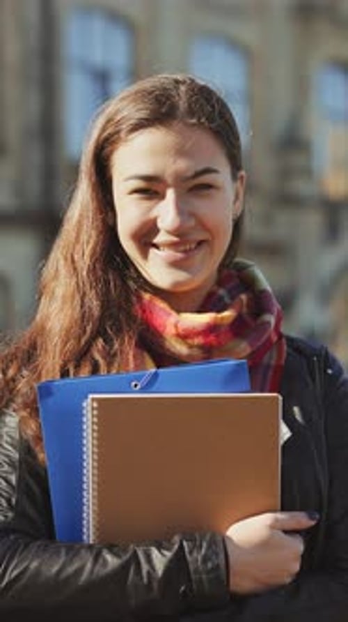 Vertical Screen Smiling Female Student with Books in Hands Standing in Front of College Building