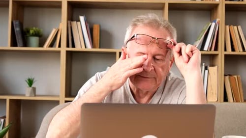Mature Man Rubbing Eyes in front of Laptop