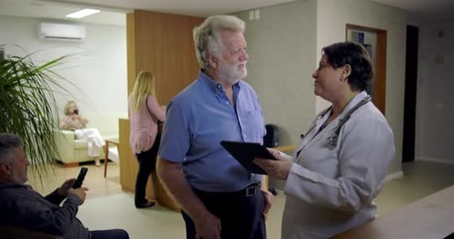 Senior man smiling while listening to female doctor explain information on digital tablet in clinic