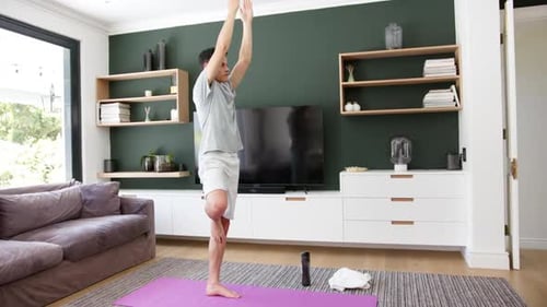 Focused biracial man practicing yoga standing on one leg in living room, copy space, slow motion