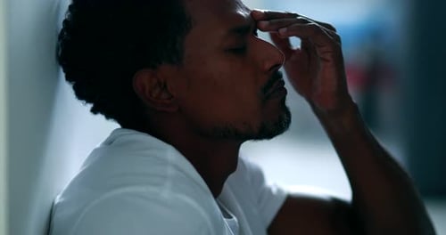 Man with Headache Sits Leaning Against Wall