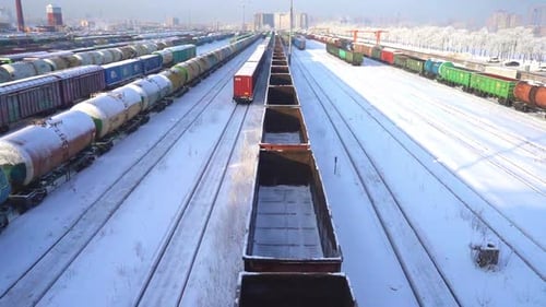 Trains and freight cars at marshalling yard in winter on sunny day with blue sky and white clouds.