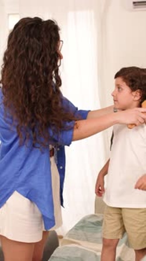 Woman brushing child's hair indoors during daytime