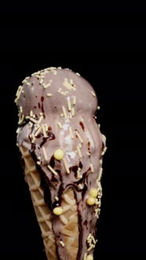 Vertical video. The chocolate ice cream scoops in the waffle cone with sugary sprinkles spin