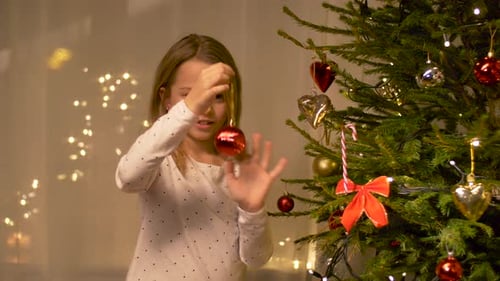 Girl Decorates Christmas Tree with Red Bauble Ornament