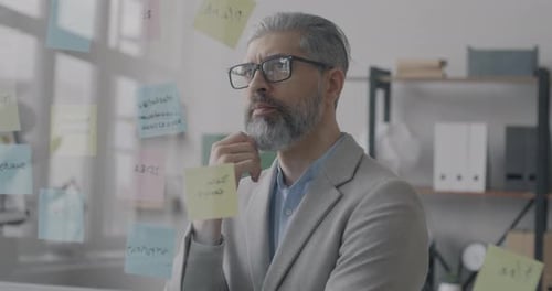 Pensive Mature Businessman Thinking Looking at Sticky Notes Focused on Problem Solving in Office
