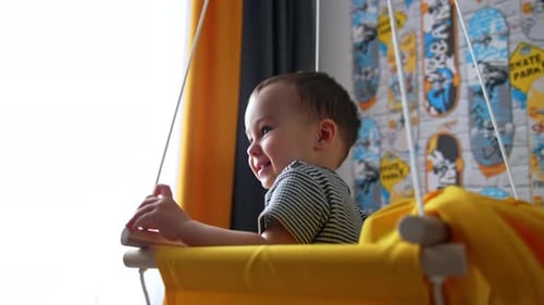 Smiling baby boy swinging in the swing. Fun time at home. Black cat comes up to a kid.