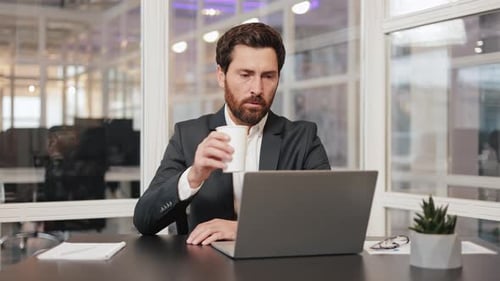 Businessman Working on Laptop in Modern Office Sipping Coffee