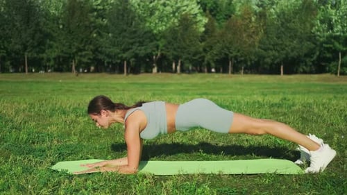 Beautiful sports girl in is engaged in stretching on a sports mat in a city park. Yoga in a sunny me