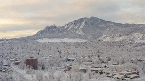 High drone shot moving right of Boulder Colorado and rocky Flatiron mountains after large winter sno