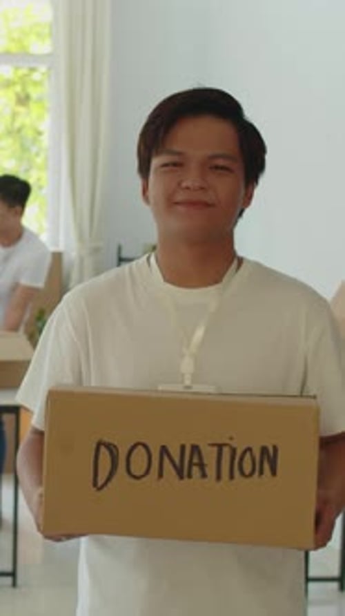 Asian Volunteer Holding Box with Collected Food and Clothes for Donation