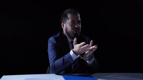 Handcuffed Man Speaking in Dark Interrogation Room
