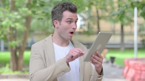 Young Man Celebrates Tablet Success in Green Park