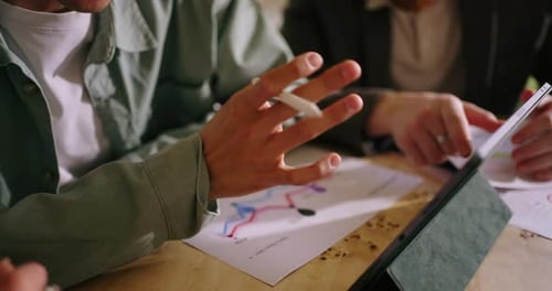 Brainstorming im Büro, Nahaufnahme von Menschen, Händen, Geräten und Papieren mit Diagrammen auf der Tischplatte