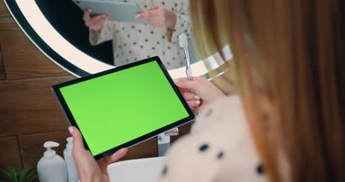 Primer plano de una mujer joven que sostiene una tableta con pantalla verde en sus manos. Vista trasera de la mujer